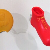 Red boot-shaped kazoo toy with yellow laces, next to a yellow souvenir coin—possibly Ronald McDonald-themed. Equal parts kazoo whimsy and fast food fever dream.