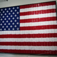 American flag constructed entirely from rows of red, white, and blue plastic kazoos arranged on a black wall—thirteen stripes and a star field recreated with kazoo chaos and patriotic commitment.
