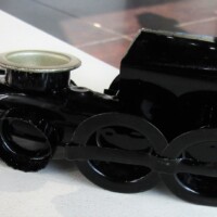 Glossy black toy train engine with a metallic silver smokestack and oversized stylized wheels—resting solo on a white surface like it’s about to toot out a kazoo solo