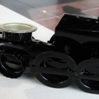 Glossy black toy train engine with a metallic silver smokestack and oversized stylized wheels—resting solo on a white surface like it’s about to toot out a kazoo solo