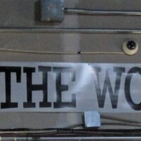 Banner hung indoors with the phrase ‘WE KEEP THE WORLD HUMMING!’ printed in bold black capital letters. The kazoo factory's mission statement, tagline, and possibly life purpose.