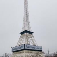 White Eiffel Tower replica with 'Bordeaux Center' sign, standing on a grassy lawn in Fayetteville, North Carolina, with power lines and pine trees in the background.