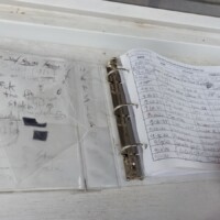 Close-up of the World's Largest Frying Pan visitor logbook as a hand turns a page, revealing handwritten entries spanning January dates.