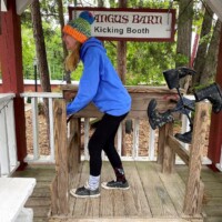 Visitor playfully braces inside the Angus Barn Kicking Booth, colorfully socked feet grounded as the boots line up for comedic impact.