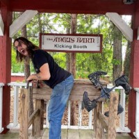 A visitor leaning into the Angus Barn Kicking Booth, positioned in front of swinging leather boots for a lighthearted photo-op