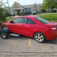 A red compact car hitched to a tow dolly in a parking lot