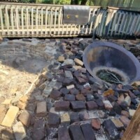 Brick-lined circular fire pit set into a multicolored brick patio, surrounded by a wooden fence and adjacent to a metal-sided building at DeLeon Springs.