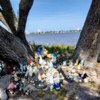 Cluster of whimsical gnome decorations surrounding a tree facing the shoreline.