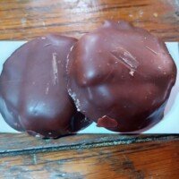 Two chocolate-covered round treats on a white plate on a wooden table