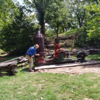 Vintage stationary engine display near Fantastic Caverns in Springfield, Missouri, with a visitor examining historic machinery in a wooded outdoor exhibit.