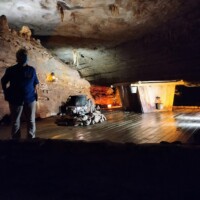 Underground scene at Fantastic Caverns in Springfield, Missouri, featuring rugged cave walls, a circular stone structure, and a warmly lit wooden cabin nestled inside the cavern.