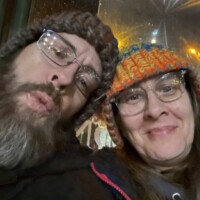 Nancy and Zach sitting together in the bus at night, faces softly blurred, surrounded by reflections and quiet road light.
