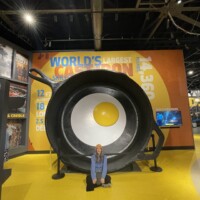 Nancy kneeling in front of the world’s largest frying pan exhibit, featuring a giant egg and bold measurements in a roadside museum