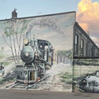 Welcome to Holly mural featuring steam locomotive, vintage car, rustic barn, and pond with ducks, celebrating small-town charm and history.