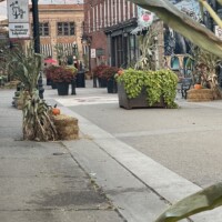 Downtown Holly Michigan fall street scene with decorated storefronts, hay bales, pumpkins, and string lights creating a festive small-town atmosphere