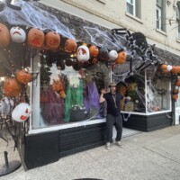 Downtown Holly Michigan storefront decorated for Halloween with jack-o'-lanterns, cobwebs, costumes, and giant spider, capturing festive fall spirit.