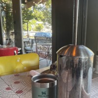 Table at The Laundry Restaurant in Fenton Michigan with French press and metal ‘Stanley’ coffee cup, red and white patterned tablecloth, and view of indoor and outdoor seating