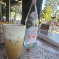 Table at The Laundry Restaurant in Fenton Michigan with iced cold brew topped with salted caramel cold foam and Acqua Panna water bottle on red and gray leaf-patterned surface.