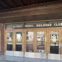 Entrance to Detroit Model Railroad Club in Holly Michigan with double wooden doors, glass panels, and seasonal schedule poster showing open months