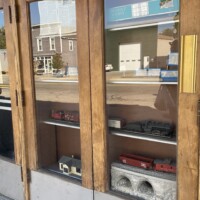 Detroit Model Railroad Club window display in Holly Michigan featuring red and black model trains, train tunnel, and miniature building with street reflections in glass