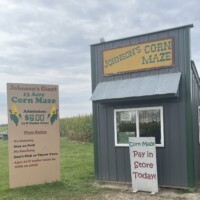 Entrance to the corn maze at Johnson’s Pumpkin Farm in Michigan, with the admission sign and the cornfield visible behind the small maze building.