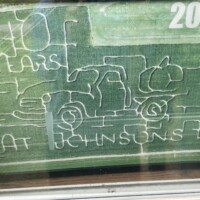 A printed aerial diagram of the 2025 corn maze at Johnson’s Pumpkin Farm. The maze design outlines a pickup truck carrying a pumpkin and includes the text “40 years at Johnson’s.” The image is displayed behind glass.