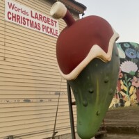 The World’s Largest Christmas Pickle statue wearing a Santa hat at Christmas Winter Wonderland in Fort Smith, Arkansas, photographed during dusk with the building and sign in the background.