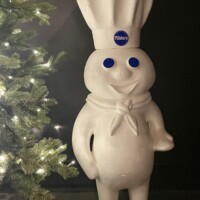 Large Pillsbury Doughboy statue with blue eyes and chef hat standing beside a lit Christmas tree at Christmas Winter Wonderland in Fort Smith, Arkansas.