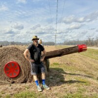 Zach standing next to hay bale cannon sculpture at Jim Bird's Hay Bale Art in Forkland Alabama