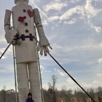 Nancy standing at base of 35-foot tall Tin Man sculpture at Jim Bird's Hay Bale Art in Forkland Alabama