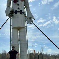 Zach standing at base of 35-foot tall Tin Man sculpture at Jim Bird's Hay Bale Art in Forkland Alabama