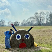 Nancy standing next to hay bale reindeer sculpture with googly eyes at Jim Bird's Hay Bale Art in Forkland Alabama
