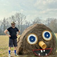 Zach standing next to hay bale sculpture with oversized googly eyes at Jim Bird's Hay Bale Art in Forkland Alabama