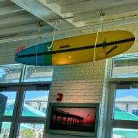 Sunrise surfboard hanging from the ceiling inside Salt Life Food Shack with a coastal sunset pier photo on the wall below in St. Augustine Beach Florida