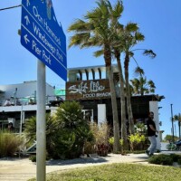 Blue directional sign pointing to Ocean Hammock, Windswept Park, and Pier Park with Salt Life Food Shack visible in the background in St. Augustine Beach Florida