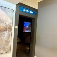 Doorway to 'The Man Cave' room at Furnitureland South, marked by a neon sign above the entrance, with a TV playing sports visible inside.