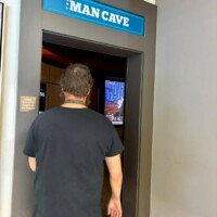 Zach walks into the Man Cave entrance at Furnitureland South, with the lit-up sign above the doorway and a TV visible inside.