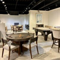 Showroom floor in the Furnitureland South outlet, featuring a round wood game table with chairs, a billiards-style table, and other dining and seating displays