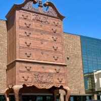 Close-up of the World's Largest Highboy Dresser's drawers and ornate broken pediment top, with parked cars and the Furnitureland South building below
