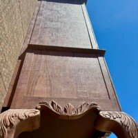 Looking straight up the side of the World's Largest Highboy Dresser, showing the carved scalloped edge of the tabletop against the tall wooden body above