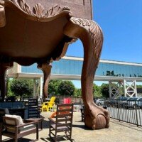 Close-up of one carved cabriole leg of the World's Largest Highboy Dresser, showing the ball-and-claw foot and acanthus leaf detailing, with outdoor patio furniture and a glass skybridge in the background.