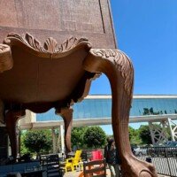 A woman looks up at the underside of the World's Largest Highboy Dresser, standing next to its oversized carved leg on the outdoor patio.