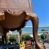 A woman in a beanie walks past the enormous carved leg of the World's Largest Highboy Dresser, highlighting the scale of the ball-and-claw foot beside her