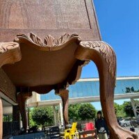 A woman pauses beneath the towering carved leg of the World's Largest Highboy Dresser, the massive foot rising well above her head.