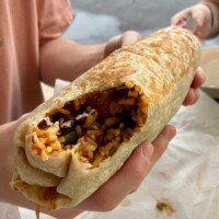 Mason holding the cut-open Shack Burrito, revealing jerk shrimp, rice and beans, aioli, and black bean and corn salsa.