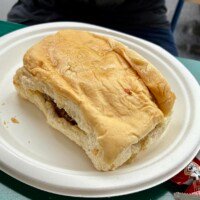 Carib Shack Fried Chicken Sandwich resting on a white plate, with crispy chicken visible between the coco bread.
