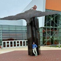 Nancy standing calmly beneath the World's Largest Bronze Falcon outside the Stroh Center