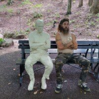 Zach sitting among ghostly white plaster figure sculptures on a park bench at Crystal Bridges Museum, again