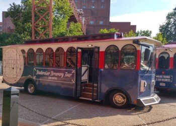 The Budweiser Brewery Tour trolley bus parked on the Anheuser-Busch campus, with the historic brewhouse building visible behind it.