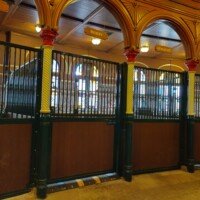Ornate Clydesdale stable stalls at Anheuser-Busch labeled with horse names Bill, Murry, Sergeant, and Teddy, under gold arches and stained glass.